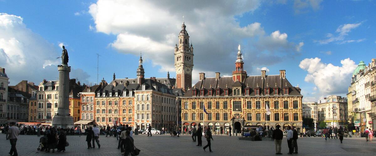 A historic square with a prominent clock tower, a statue, and ornate buildings.