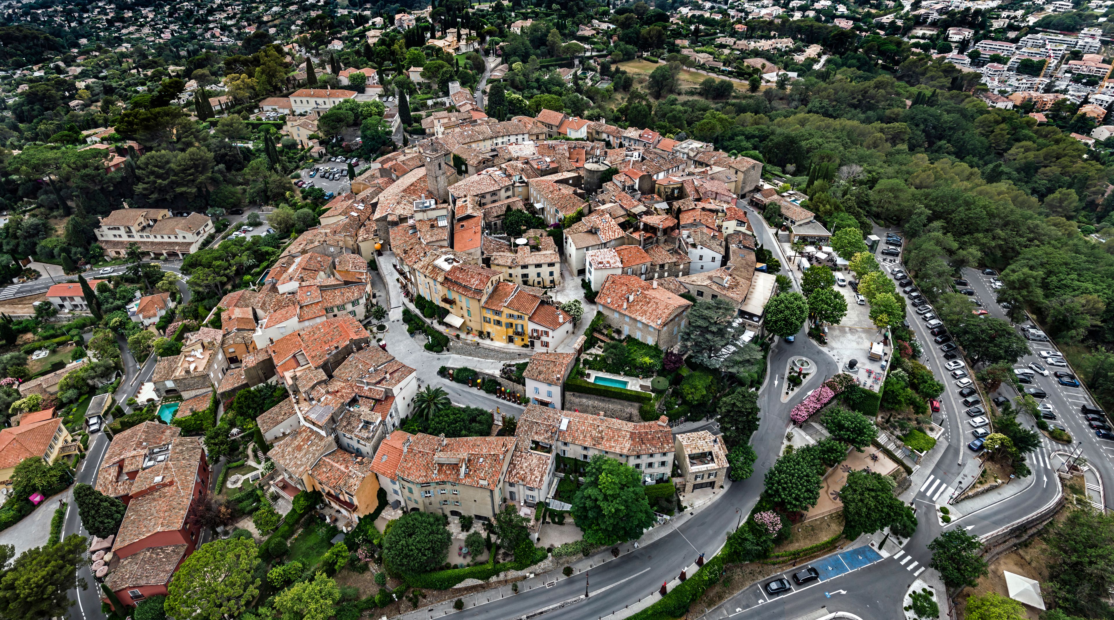 An aerial view of a historic town with a central square, narrow streets, and surrounding greenery.