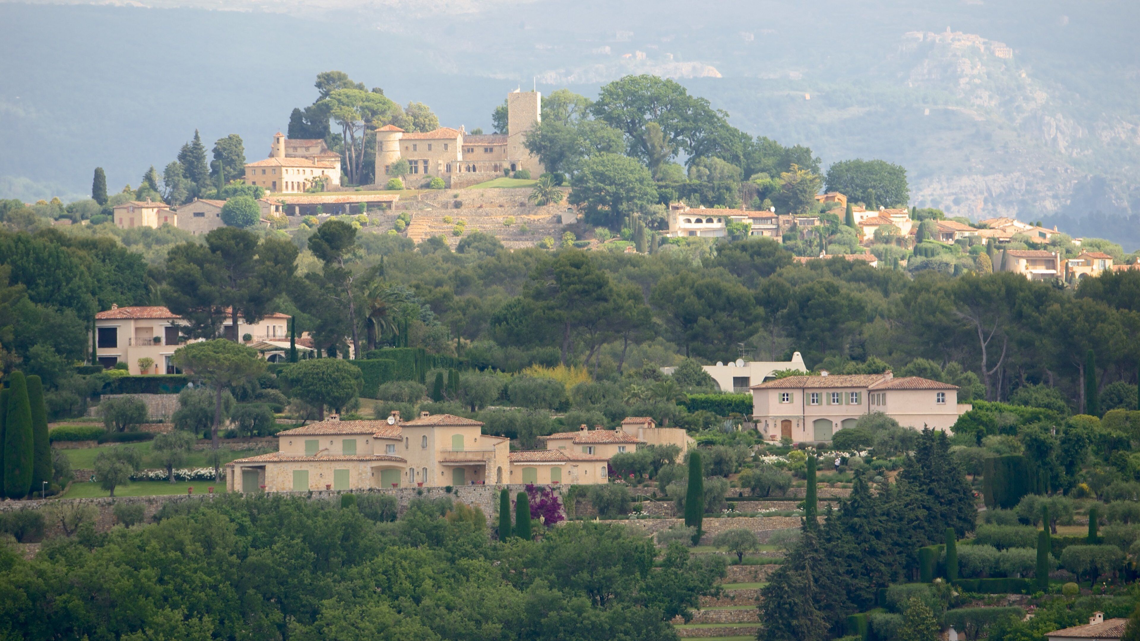 A hillside village with historic buildings, lush greenery, and a prominent tower.