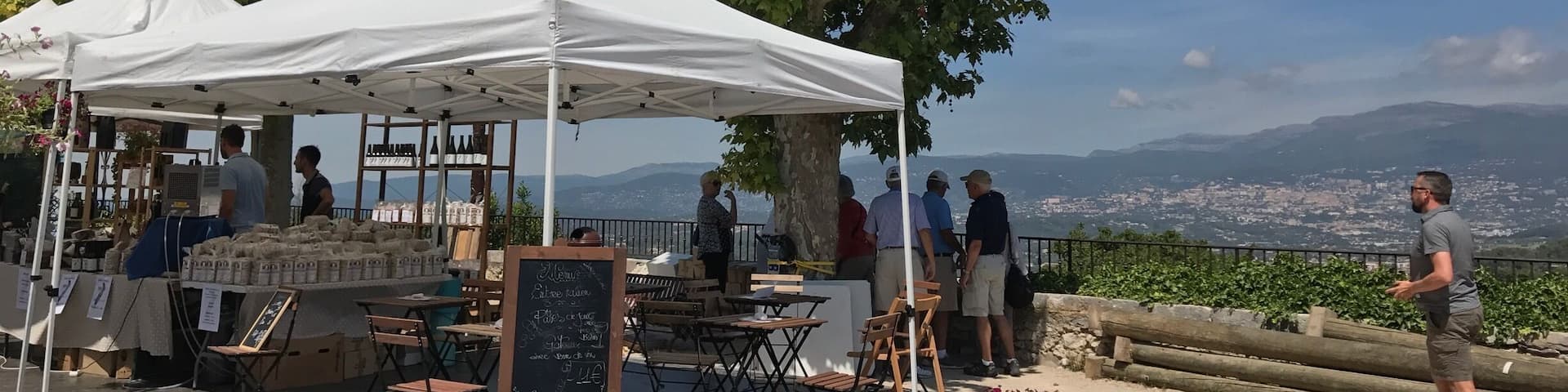 A wine tasting event with white tents and a chalkboard menu under a large tree.