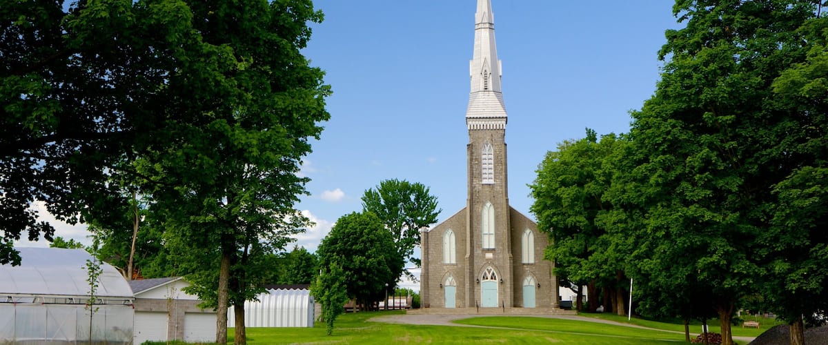 A church with a tall steeple and a cross at the top, surrounded by trees and a clear blue sky.