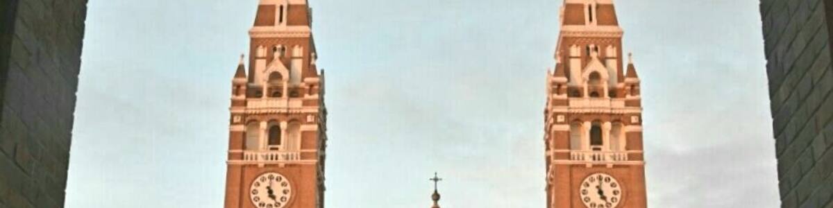 A large brick cathedral with two tall towers, each featuring a clock.