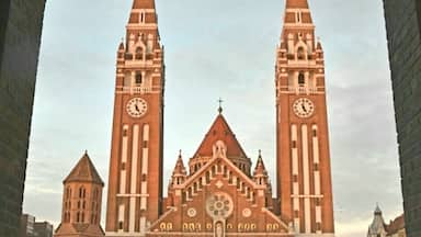 Uma grande catedral de tijolos com duas torres altas, cada uma com um relógio.