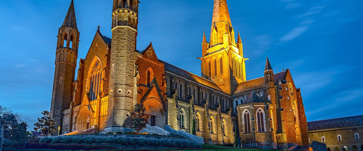 A Gothic-style cathedral with two prominent spires, a large central tower, and a well-maintained lawn in front.