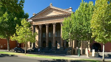 A classical building with columns, a green lawn, and a parked car.