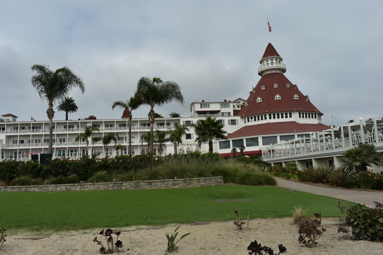 A large white building with a red roof and a tower, surrounded by palm trees and a green lawn.