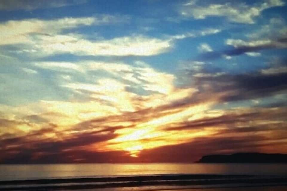 Um pôr do sol sobre uma praia com nuvens refletidas na água.