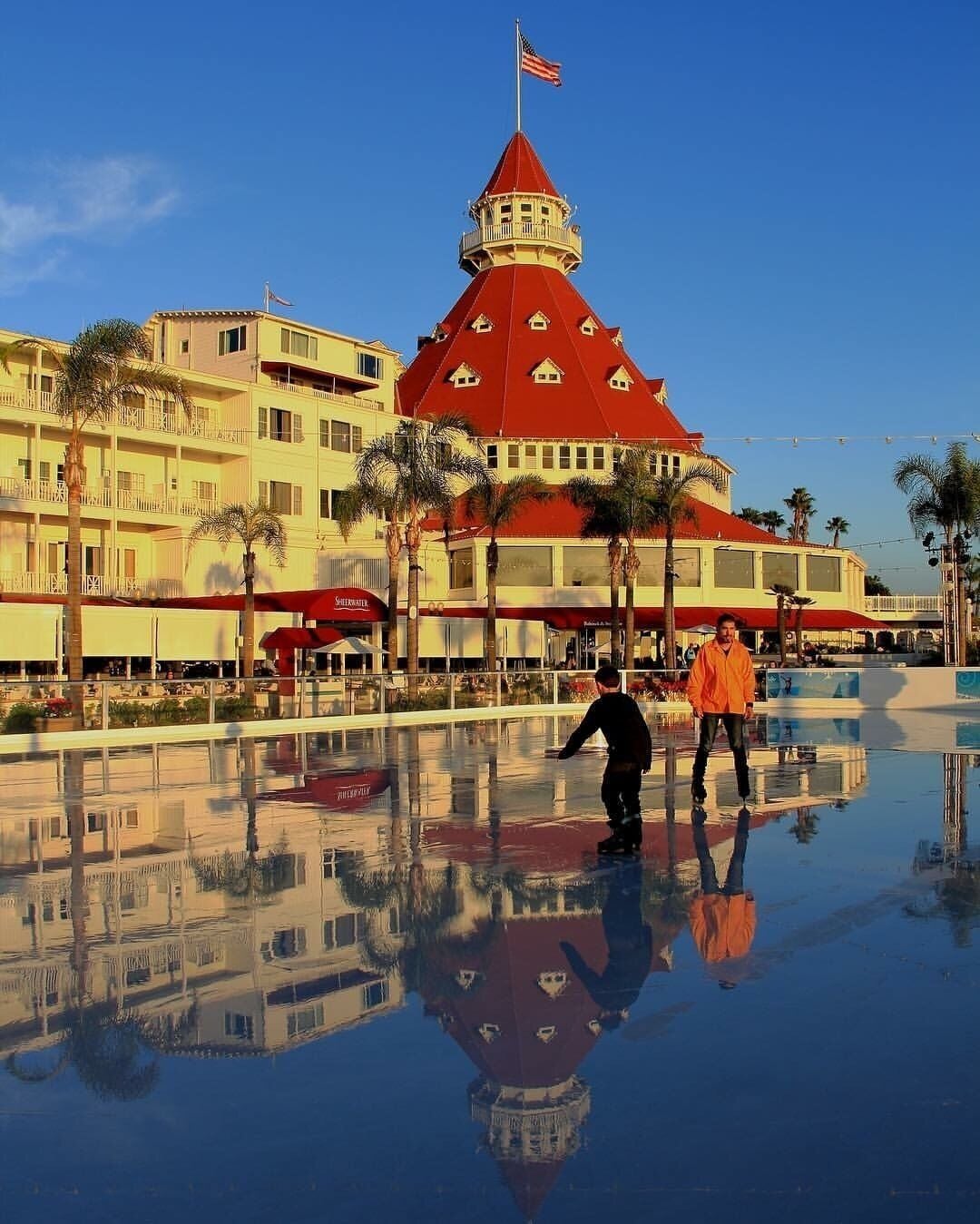A red-roofed building with a flag, palm trees, and a wet reflective surface.
