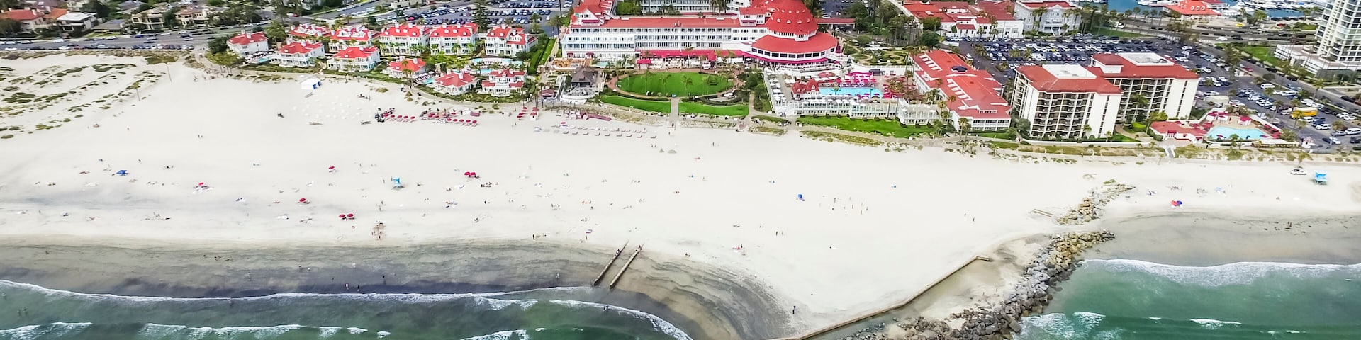 An aerial view of a coastal city with a prominent beach, marina, and a distinctive bridge.