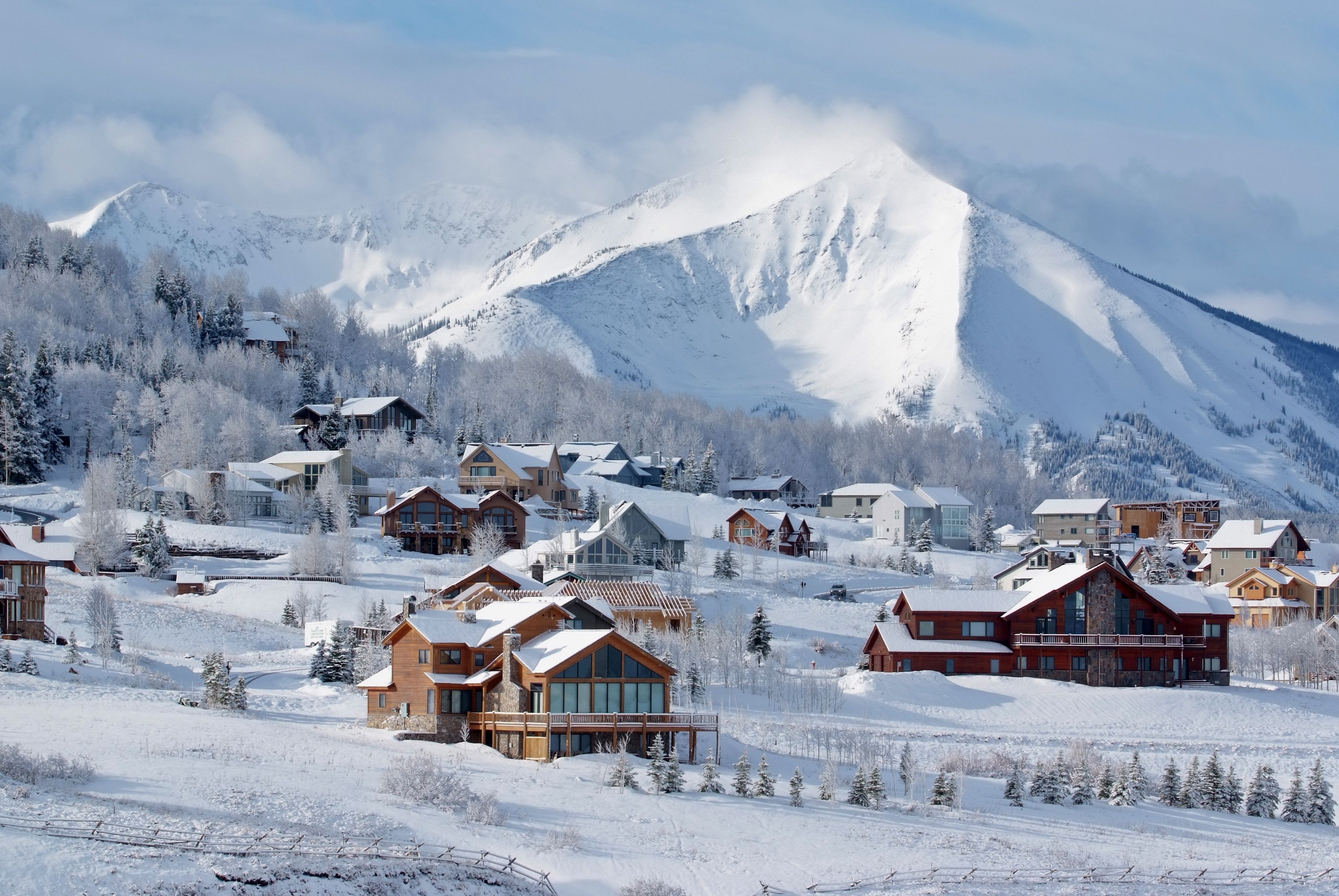 A snow-covered mountain town with wooden houses and a prominent mountain in the background.