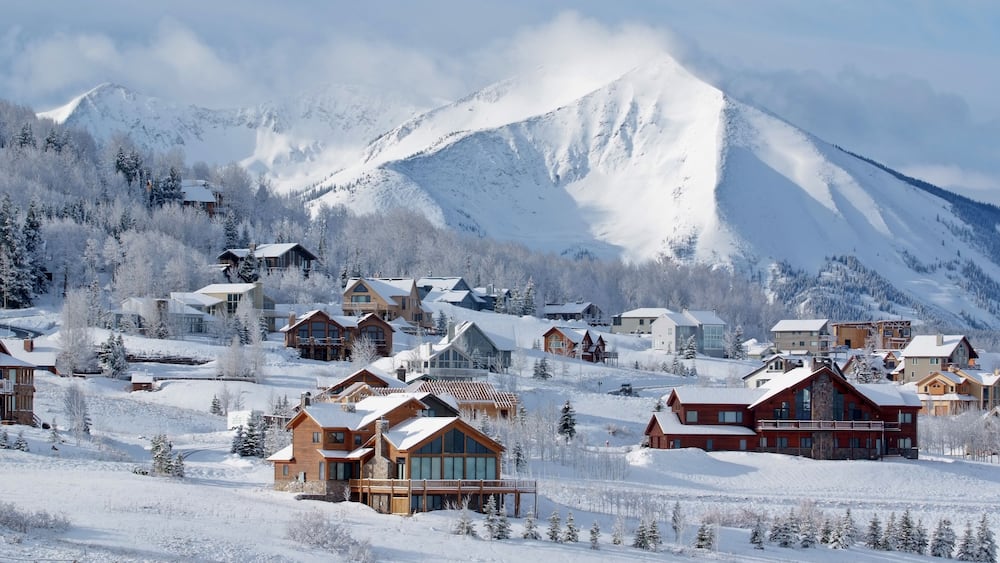 A snow-covered mountain town with wooden houses and a prominent mountain in the background.