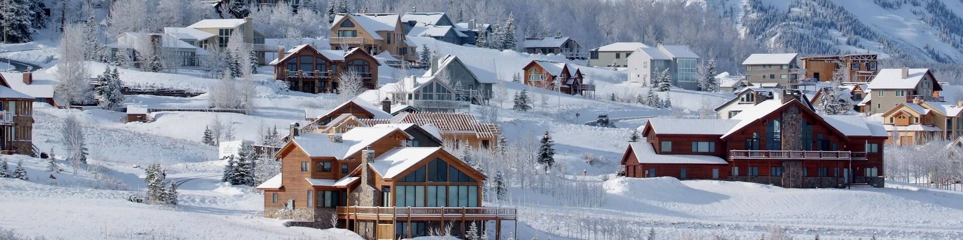 A snow-covered mountain town with wooden houses and a prominent mountain in the background.