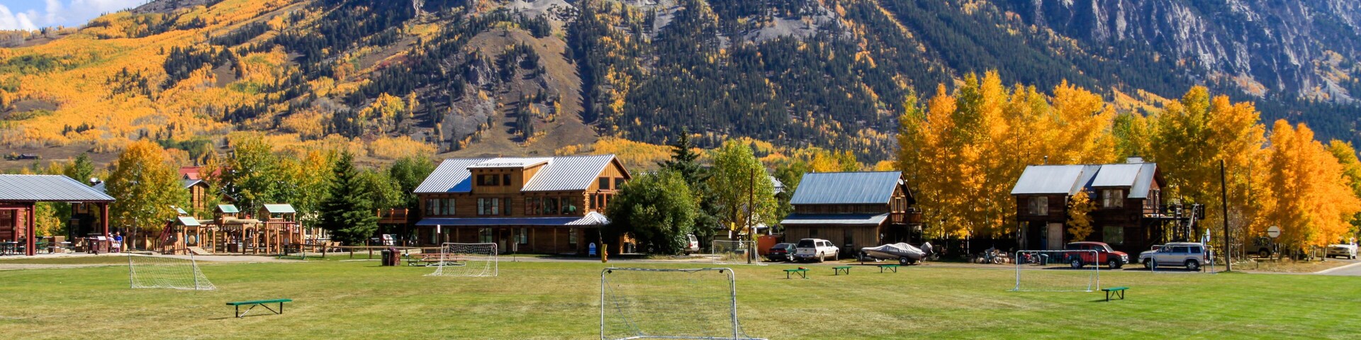 A grassy field with a soccer goal, a wooden cabin, and a mountain in the background.