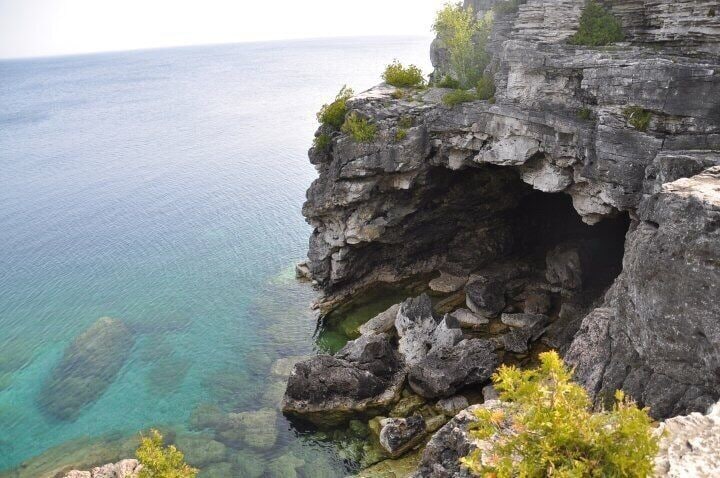 A rocky cliff with a cave entrance overlooking turquoise waters.