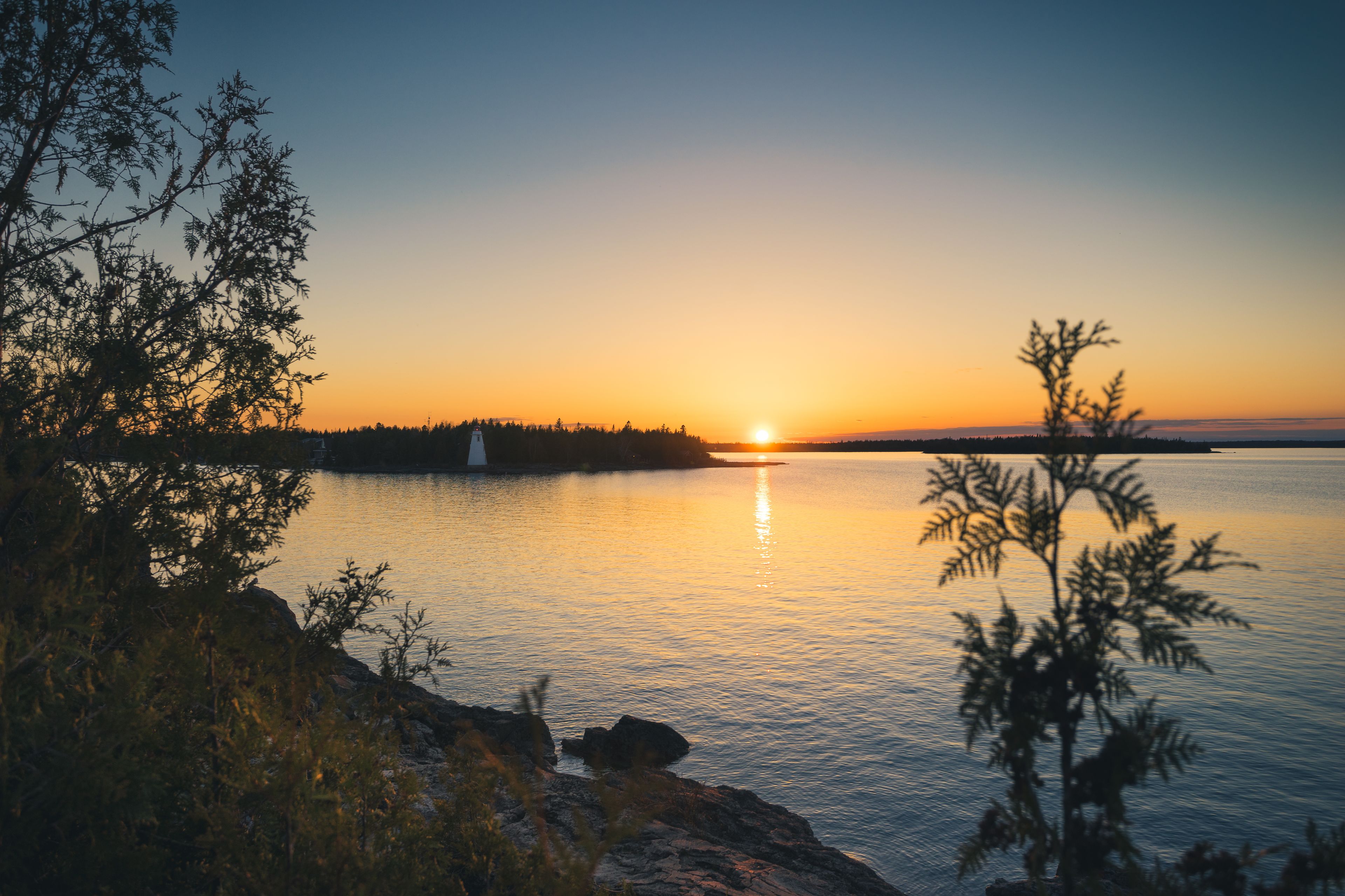 A sunset over a calm body of water with a lighthouse on a distant island.
