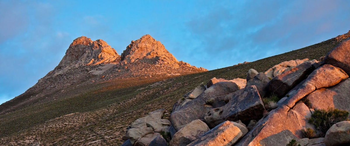 A rocky mountain landscape with large boulders in the foreground and two prominent peaks in the background.