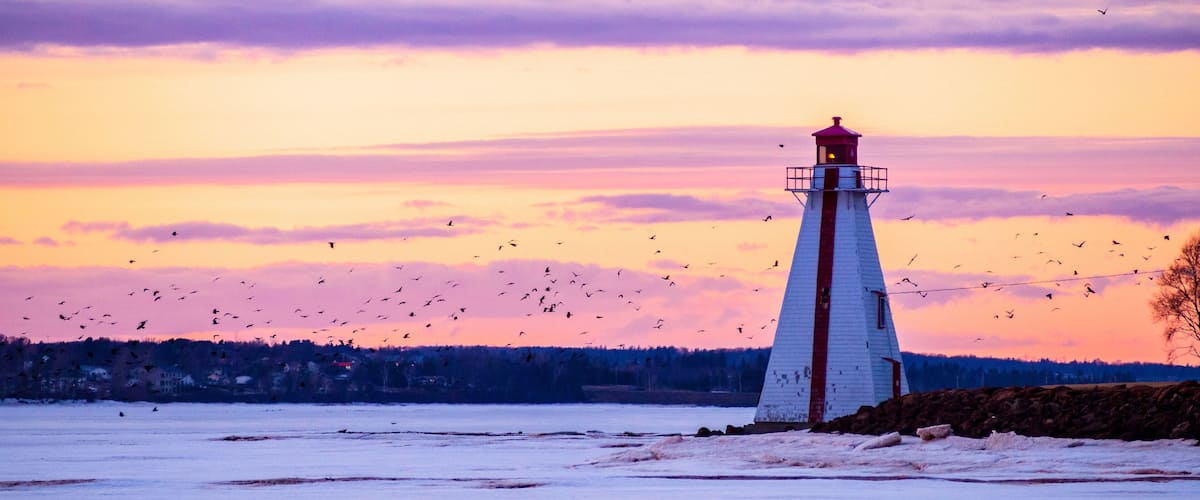A lighthouse by a frozen body of water during sunset.