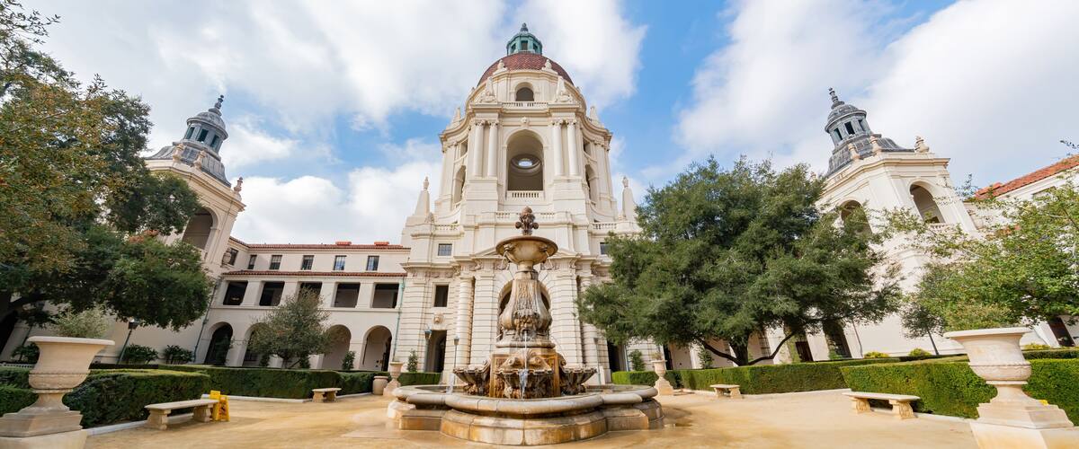 A historic building with a central fountain, surrounded by well-manicured hedges and trees.