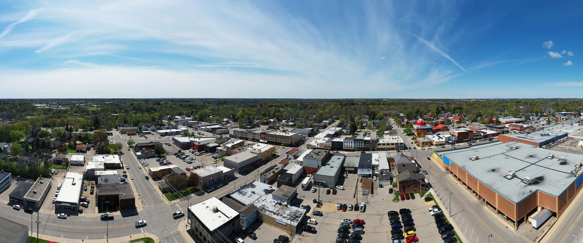 An aerial view of a town with a mix of commercial and residential buildings, a parking lot, and a large industrial building.