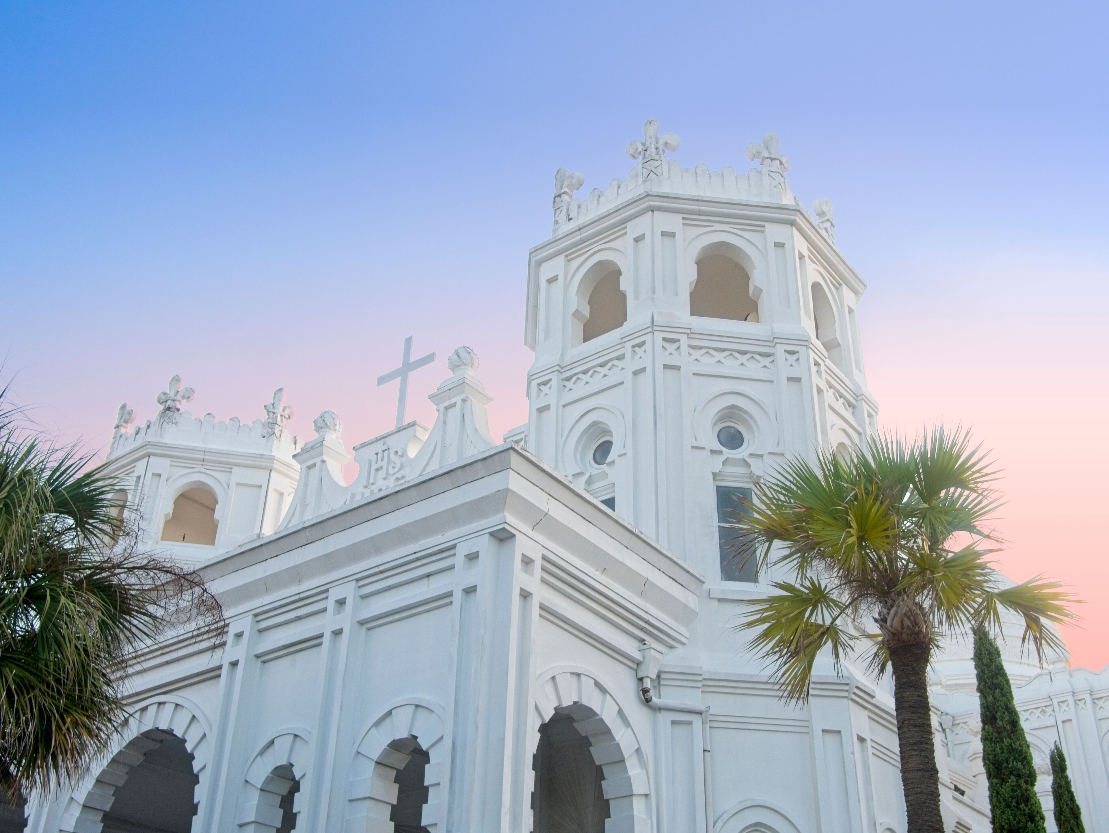 Uma igreja branca com cruz, janelas em arco e estátuas no telhado.