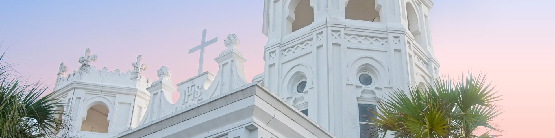 Uma igreja branca com cruz, janelas em arco e estátuas no telhado.