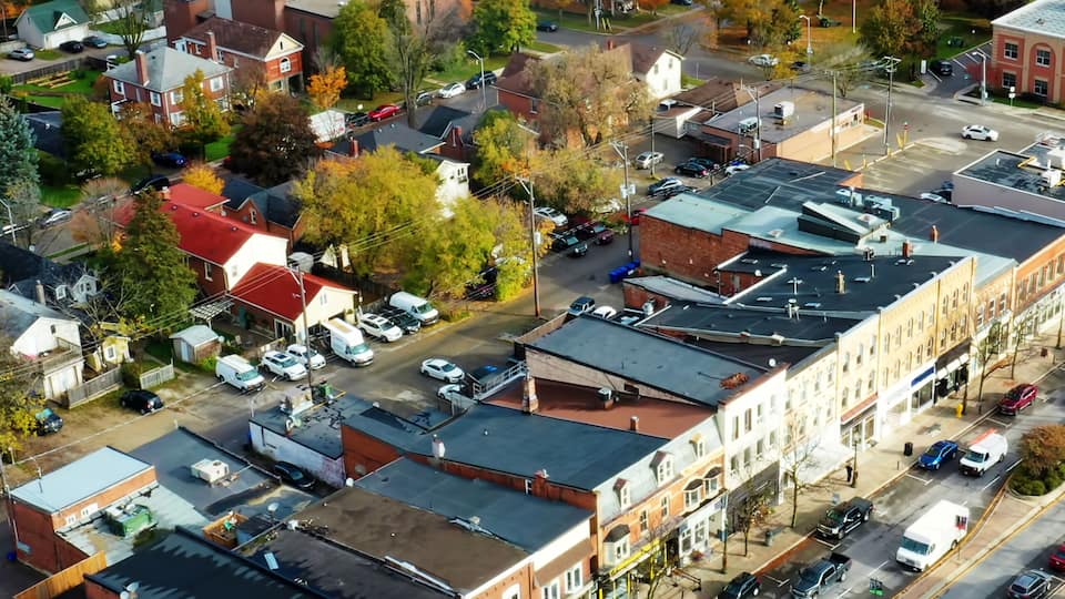 An aerial view of a town with a mix of residential and commercial buildings, a main road, and a body of water in the background.