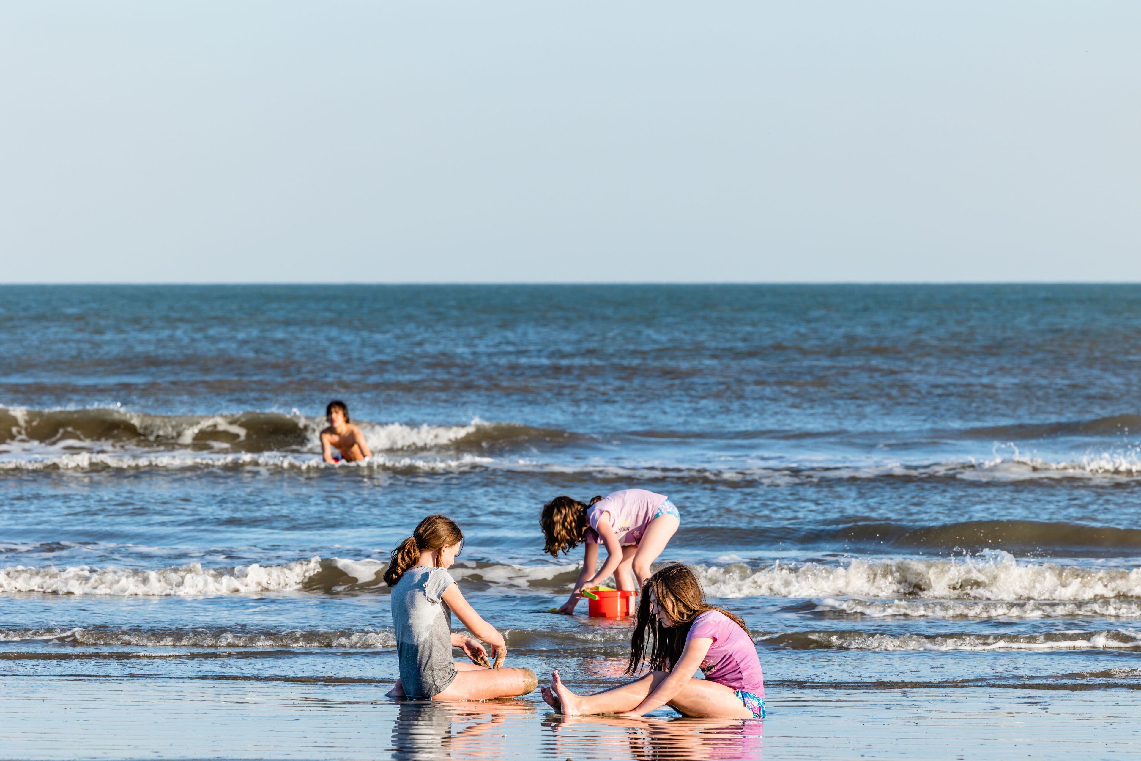 A beach with waves, people playing, and a clear sky.