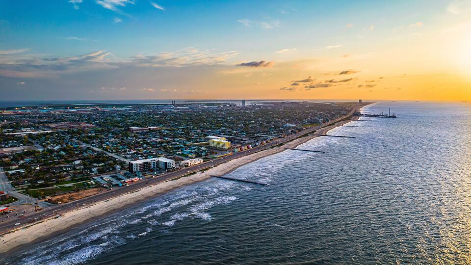 A coastal cityscape with a beach, ocean, and urban area during sunset.