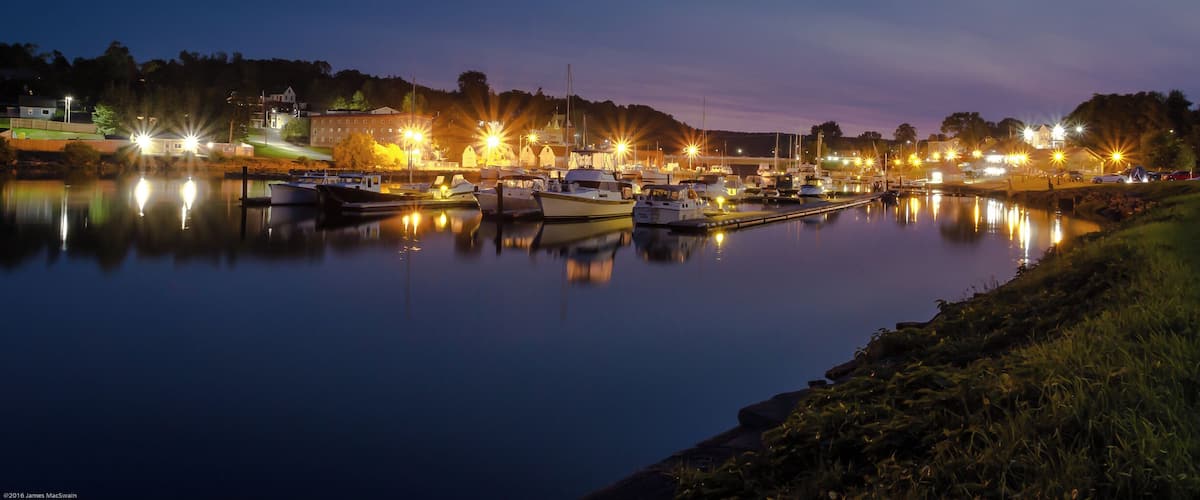 A marina at dusk with boats docked and lights reflecting on the water.