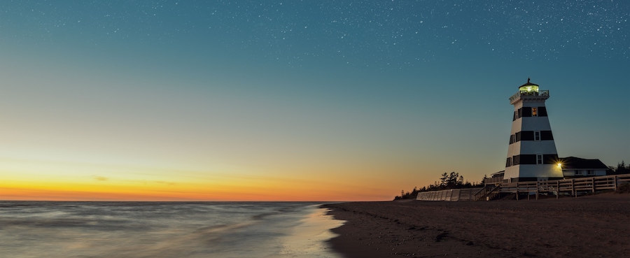 A lighthouse at sunset with a starry sky.