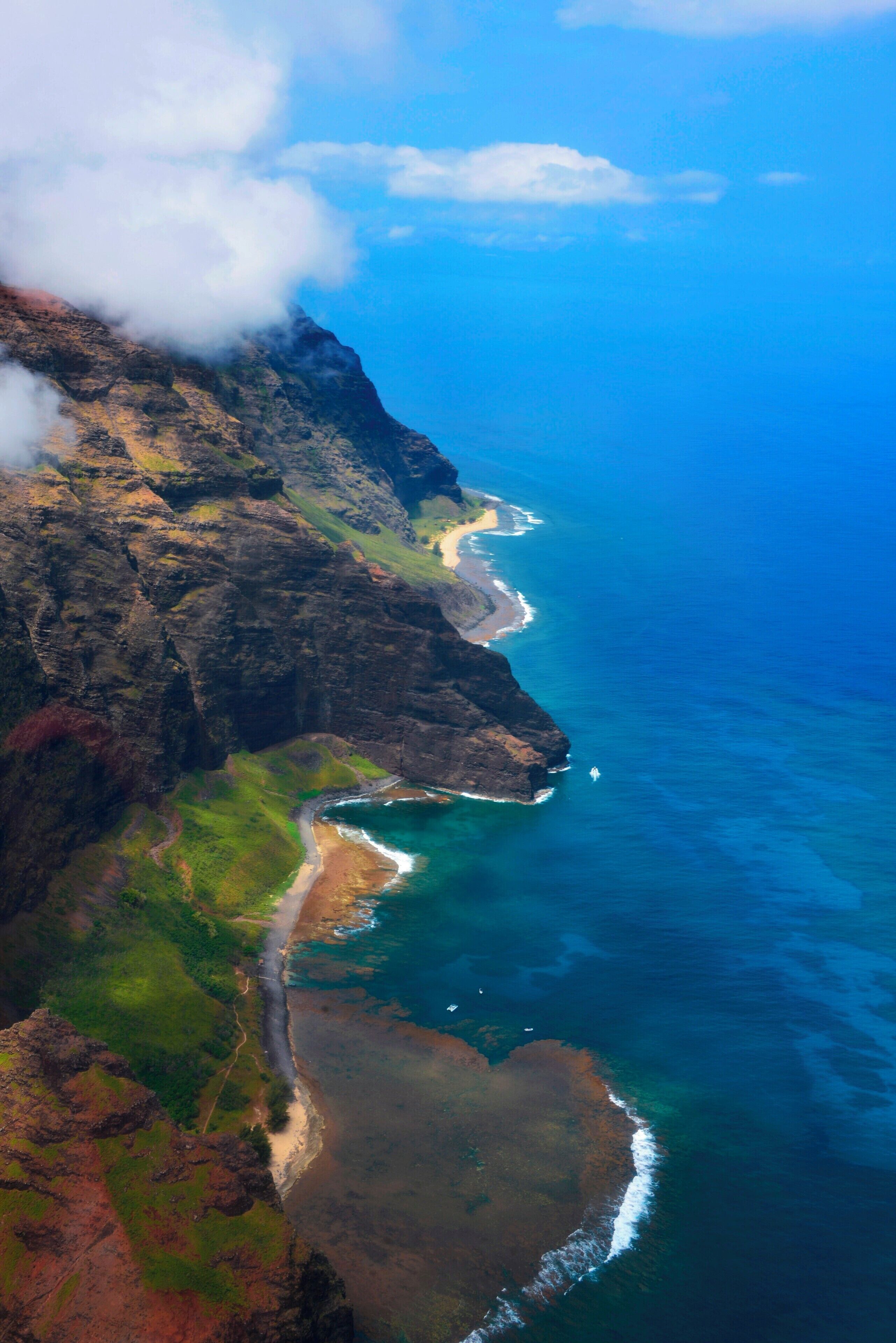 A coastal landscape with a rugged cliff, a winding road, and a beach.
