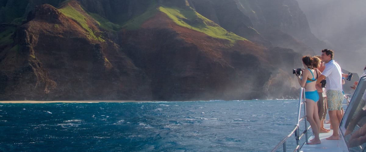 A boat with people taking photos near a mountainous coastline.
