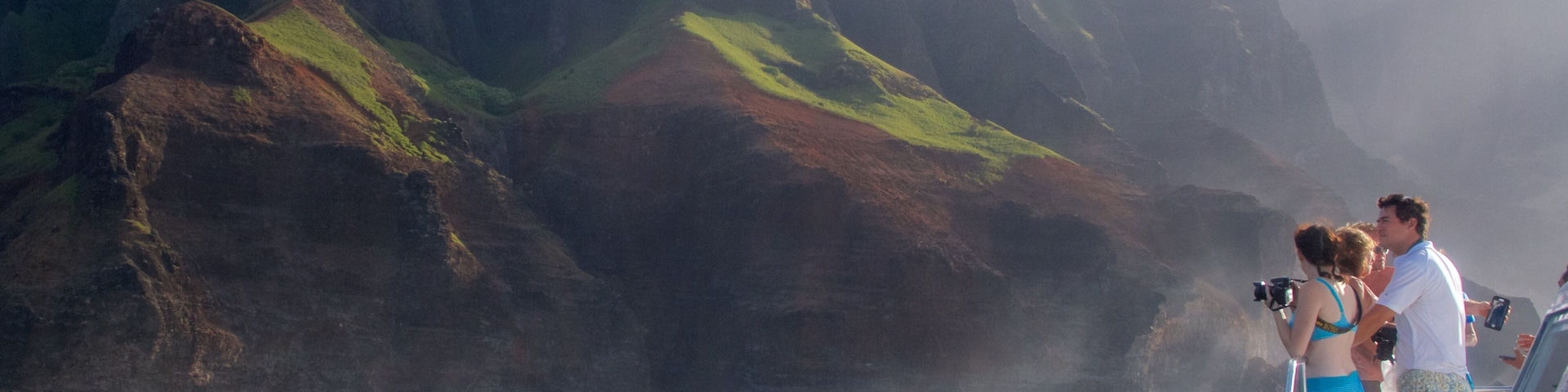 A boat with people taking photos near a mountainous coastline.