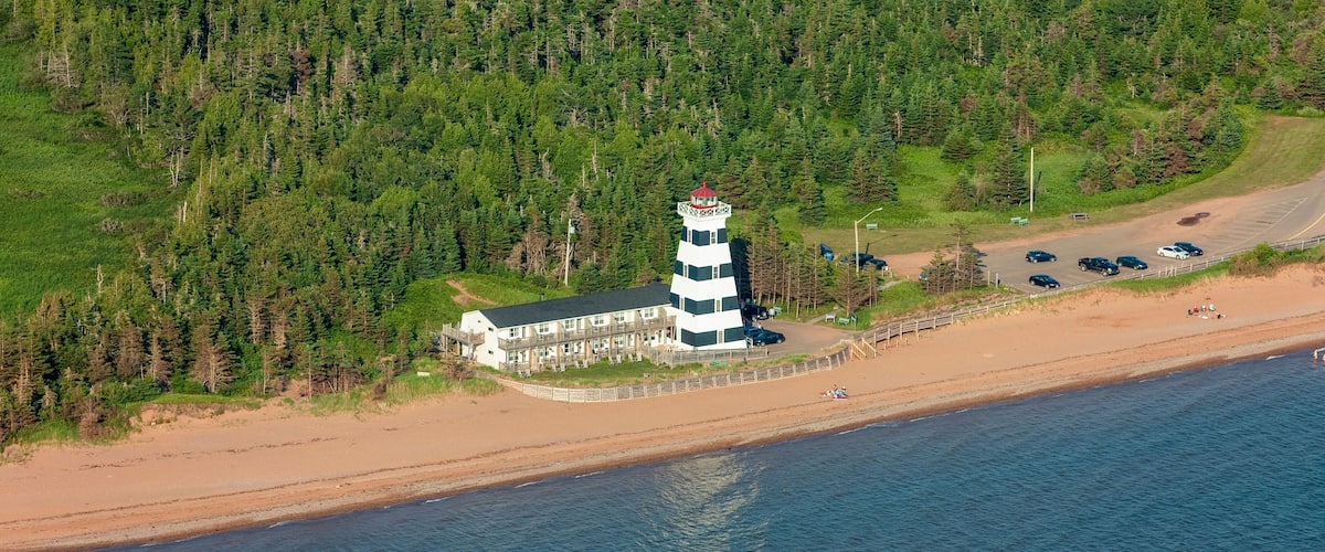 A lighthouse on a beach with a forested hill in the background.