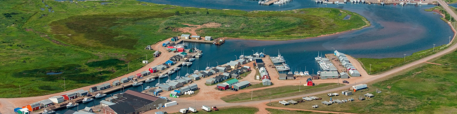 An aerial view of a coastal marina with boats, buildings, and surrounding greenery.