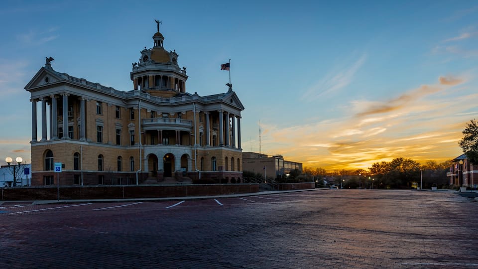 A large, historic building with a dome and columns, set against a sunset sky.