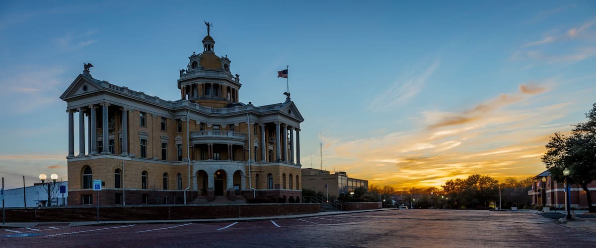 A large, historic building with a dome and columns, set against a sunset sky.