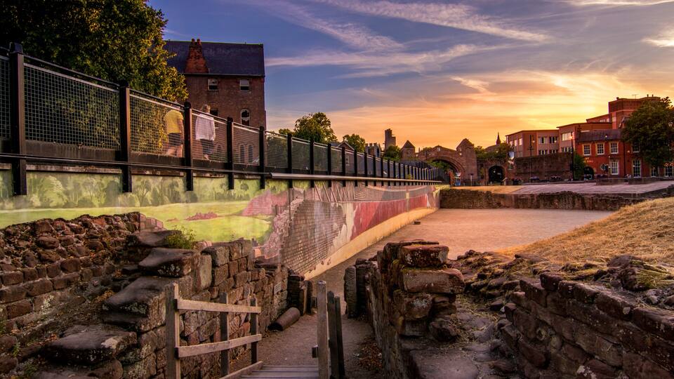 A historical site with ancient stone walls, a wooden gate, and a modern fence.