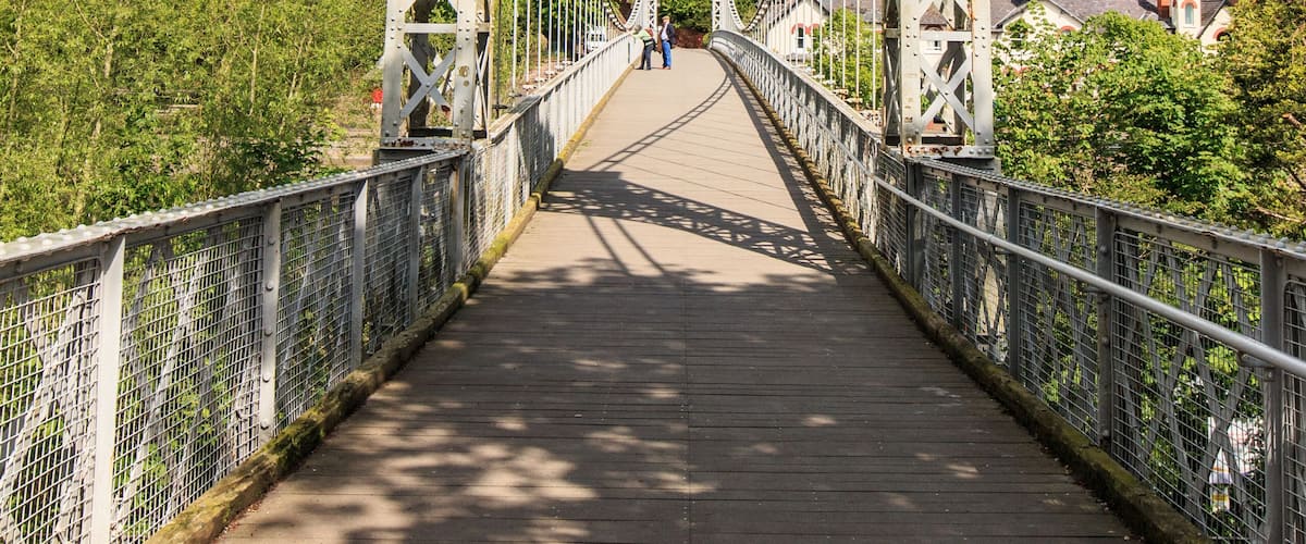A suspension bridge with a sign reading 'City of Chester Queens Park Bridge 1923.'