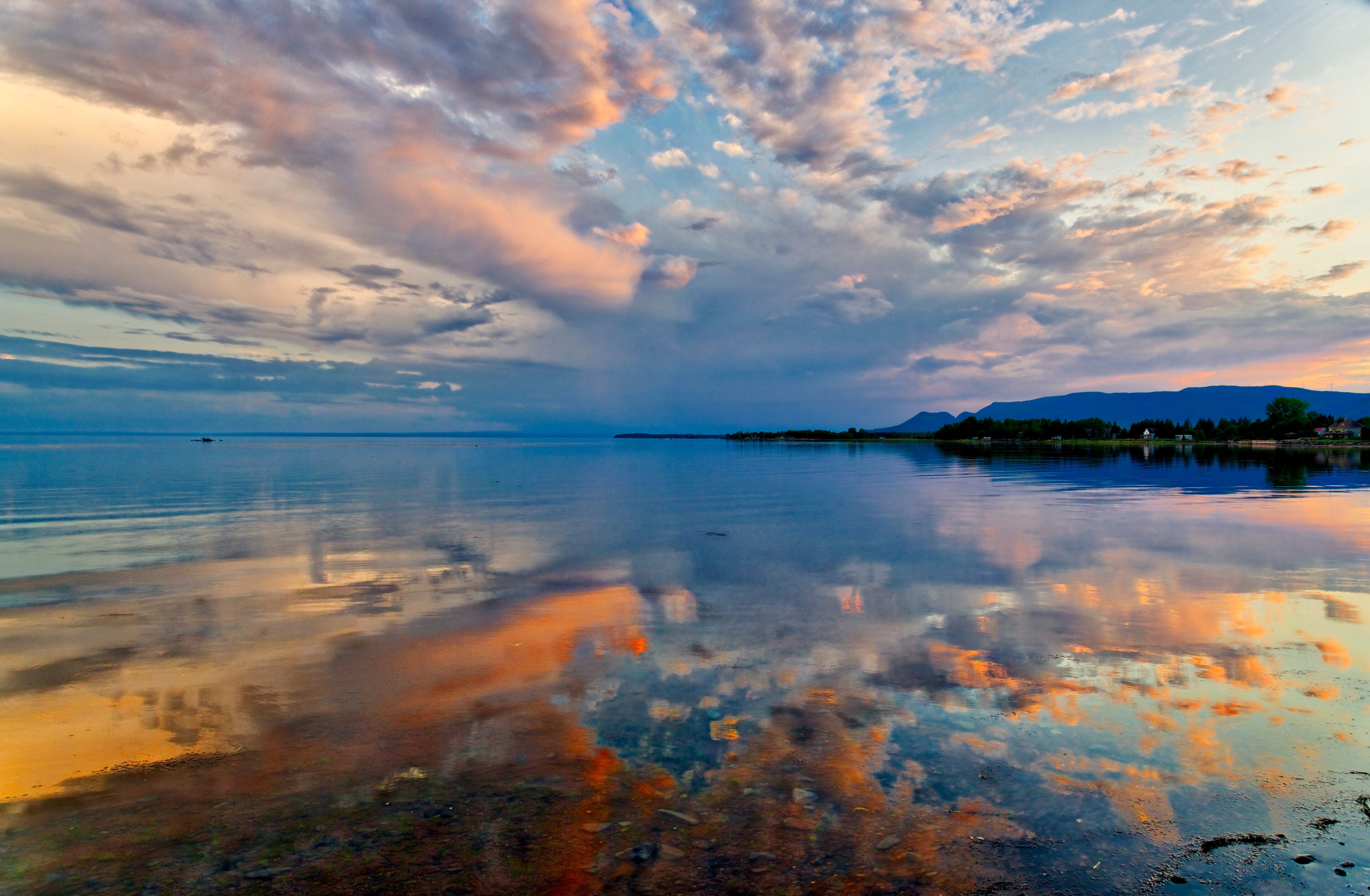 A calm lake with a reflection of the sky and mountains in the distance.