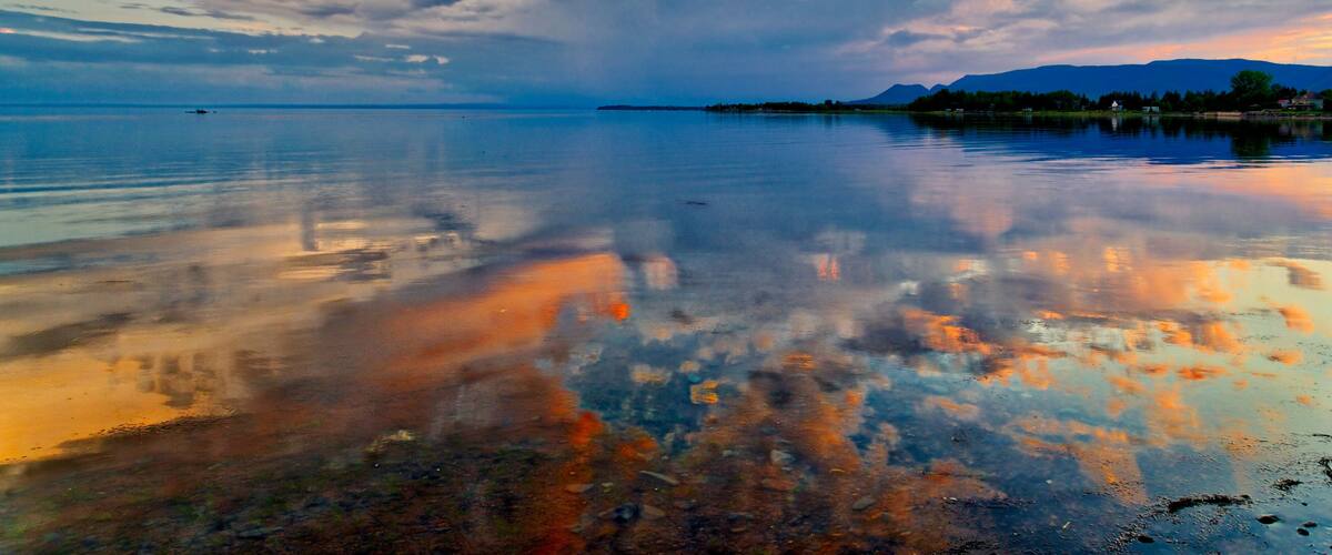 A calm lake with a reflection of the sky and mountains in the distance.