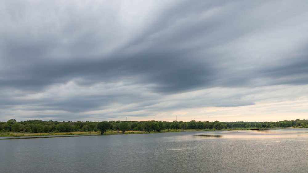 A calm lake with a cloudy sky and a forested shoreline.