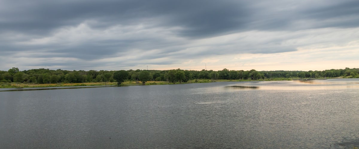 A calm lake with a cloudy sky and a forested shoreline.