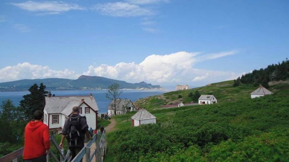 A coastal village with a wooden bridge, houses, and a distant castle by the sea.