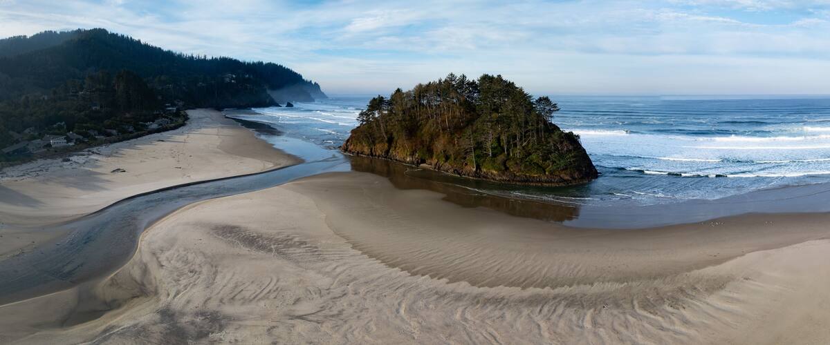A coastal landscape with a sandy beach, a rocky outcrop, and a forested hillside.