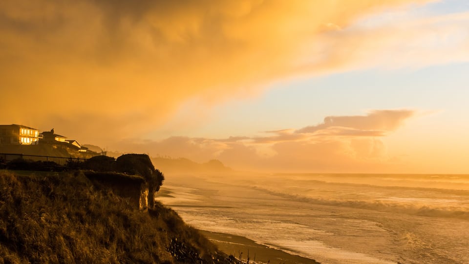 A coastal landscape with a wooden pier, grassy cliffs, and a building with illuminated windows.
