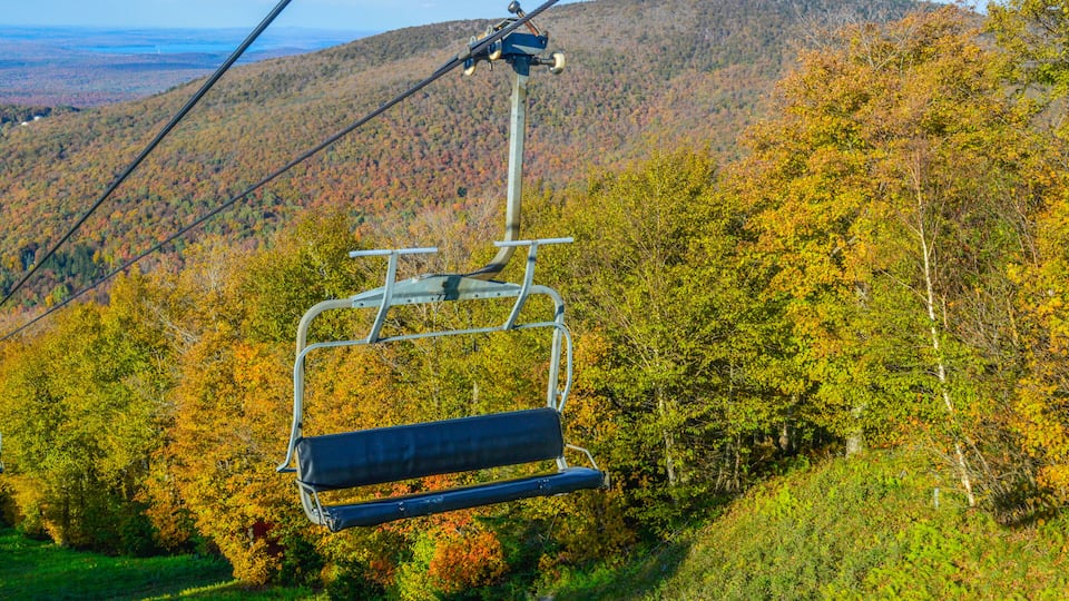 A cable car chair suspended over a forested mountain with autumn foliage.