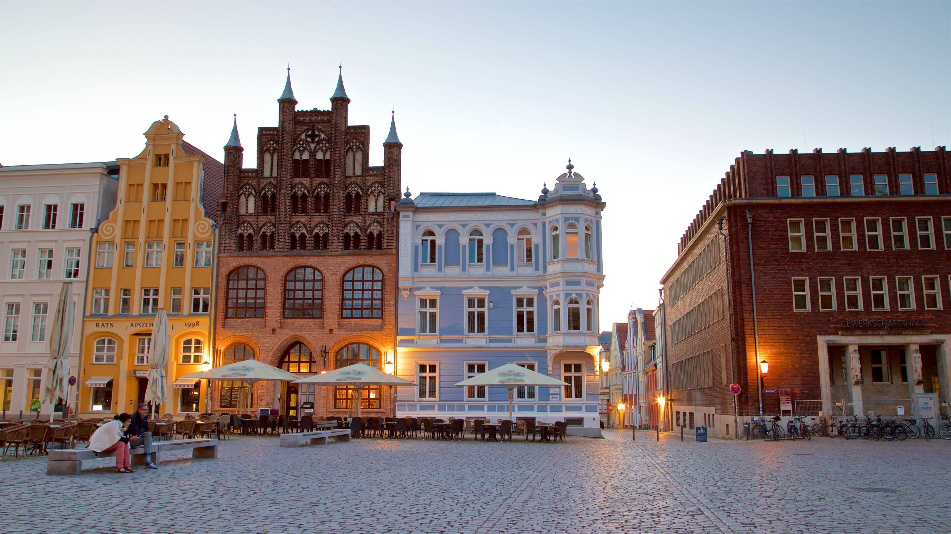 Una plaza adoquinada con edificios históricos, mobiliario exterior y bicicletas.