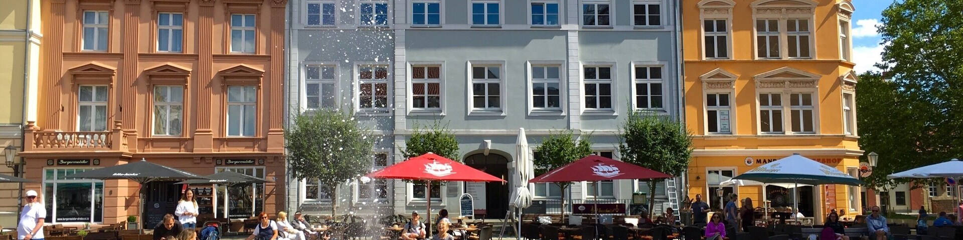 A historic square with a fountain, traditional European architecture, and outdoor seating areas.