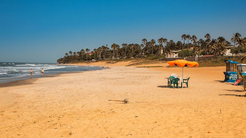 A sandy beach with palm trees, a lifeguard tower, and a few people walking.